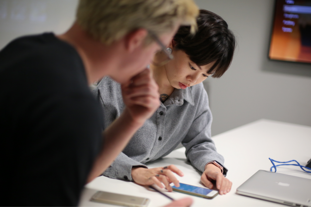 2 designers looking at a phone at a desk discussing an app